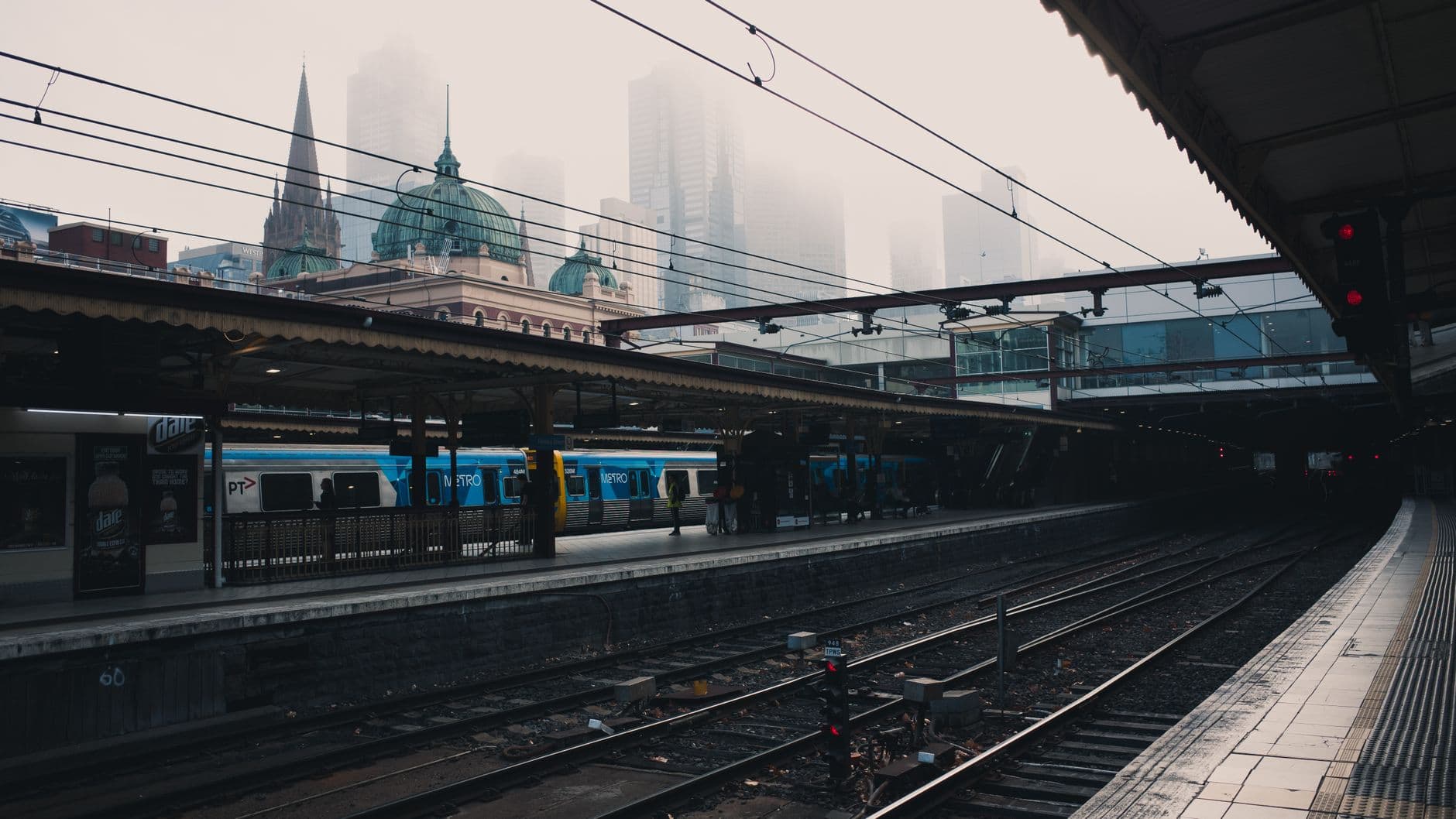 A misty view of a train station in an urban setting with trains and tracks visible.