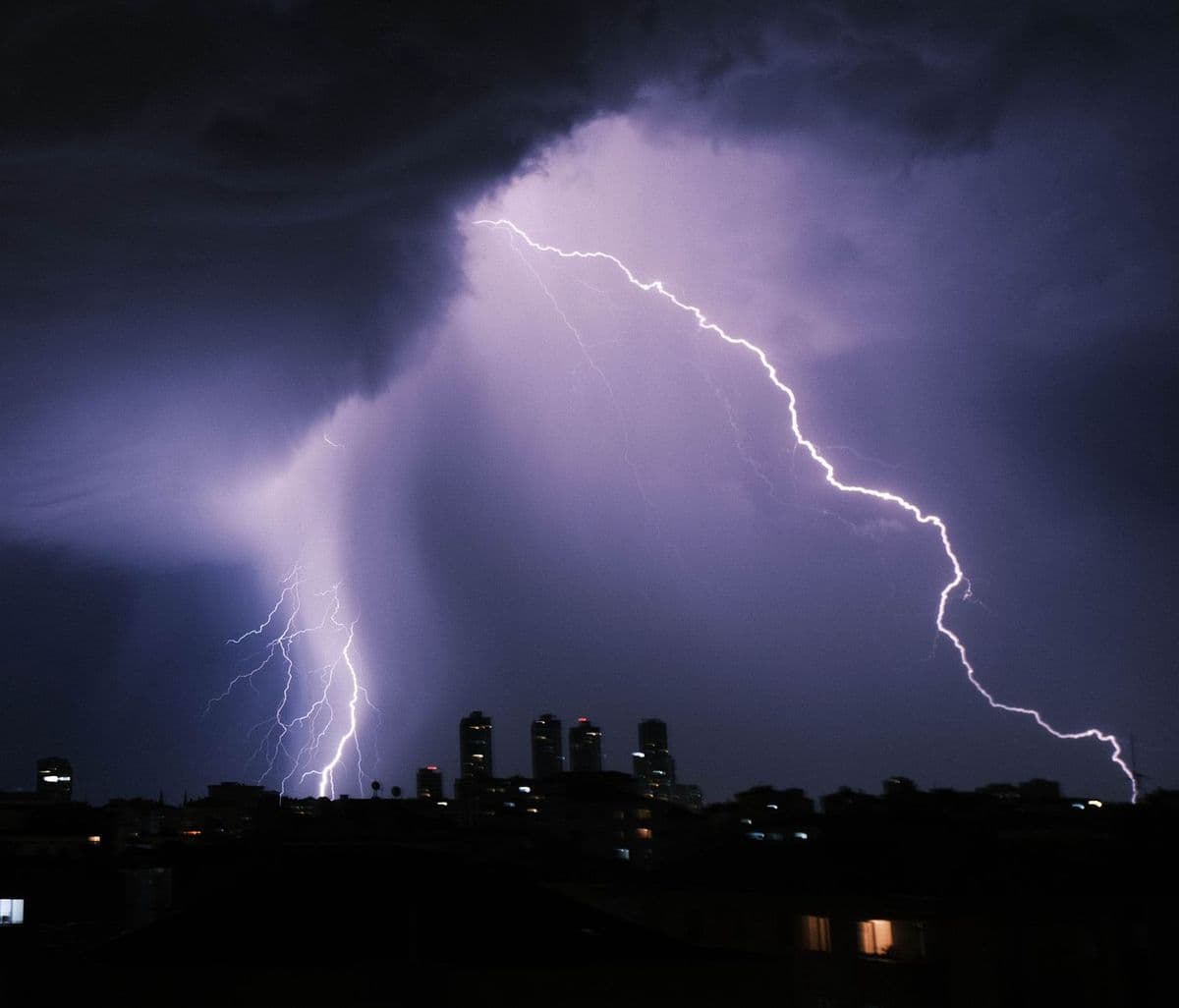 A powerful lightning bolt illuminates a city skyline during a dramatic night storm.